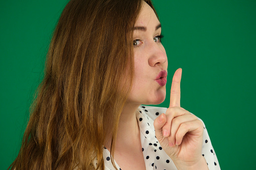Young happy woman showing silence sign finger over lips over green screen