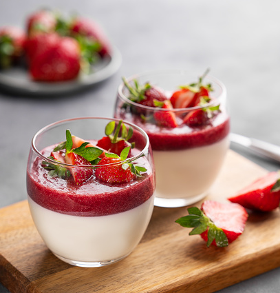 Strawberry and cream panna cotta in glasses with fresh berries on a wooden board on a gray background close up. Traditional Italian sweet dessert concept.