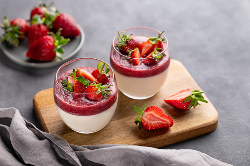 Strawberry and cream panna cotta in glasses with fresh berries on a wooden board on a gray background with napkin. Traditional Italian sweet dessert concept. Copy space.