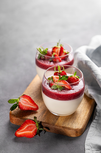 Panna cotta with strawberry and cream in glasses with fresh berries on a wooden board on a gray background with napkin. Traditional Italian sweet dessert concept. Copy space.