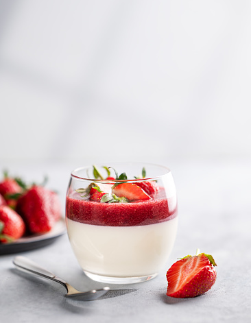 Panna cotta with strawberry and cream in glass with fresh berries on a light background close up with shadow. Traditional Italian sweet dessert concept. Copy space.