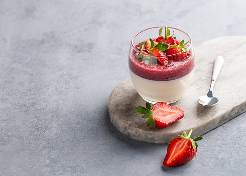 Strawberry and cream panna cotta in glass with fresh berries on a marble board on a light background with spoon. Traditional Italian sweet dessert concept. Copy space.