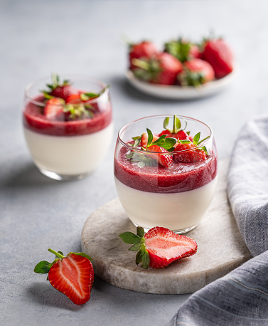 Strawberry and cream panna cotta in glasses with fresh berries on a marble board on a light background with napkin. Traditional Italian sweet dessert concept.