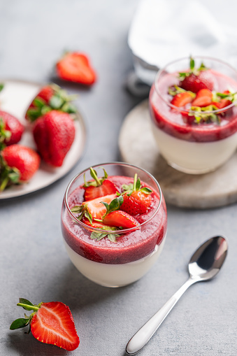 Strawberry and cream panna cotta in glasses with fresh berries on a light background. Traditional Italian sweet dessert concept.