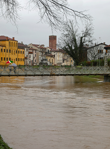 Raging river during flooding with risk of overflow and nearly submerged pedestrian iron bridge in Italy
