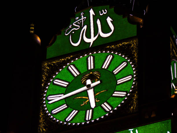 Makkah Clock Royal Tower at Night A close-up view of the Makkah Clock Royal Tower with the green color and Saudi's flag symbol at night. The translation of the Arabic text above the clock: "Allah (God) is The Greatest". makkah royal clock tower stock pictures, royalty-free photos & images