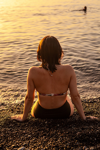 portrait of a young girl sitting at sunset by the sea in a bikini