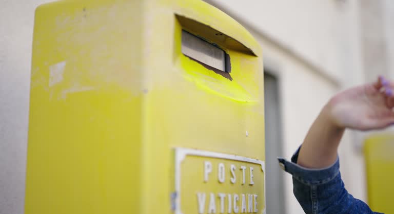 Ttourist drops postcard greetings in retro yellow post box on visit of Vatican in Rome, Italy, cinematic selective focus isolated slow motion shot