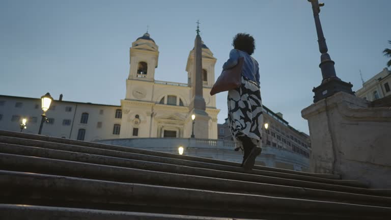 Fashion curly hair hispanic woman walks on empty staircase of the Spanish steps and holds a purse. Social media trending style of Rome Italy, travel summer tourism travel concept.