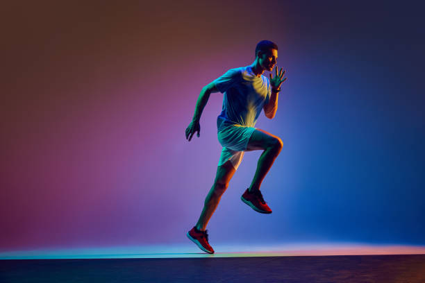 istock Young athletic man with muscular body, in headphones, training, running on gradient pink blue background in neon light 2149687898