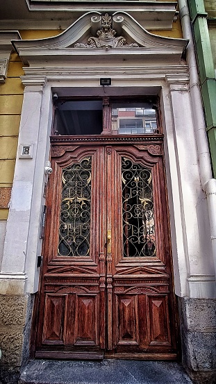 A vertical shot of an old wooden building gate with metal ornaments. The brown door with double wings has a window above.