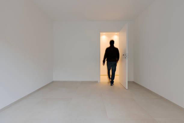 A man in an empty room comes out and is seen from behind moving. Conceptual imagery.  It is an adult walking towards the exit,