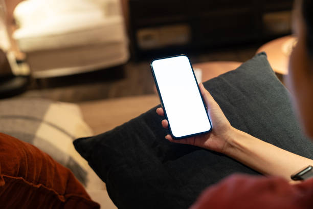 istock View from behind a person using a smartphone with a blank screen, in a warmly lit, comfortable home interior setting. 2149690138