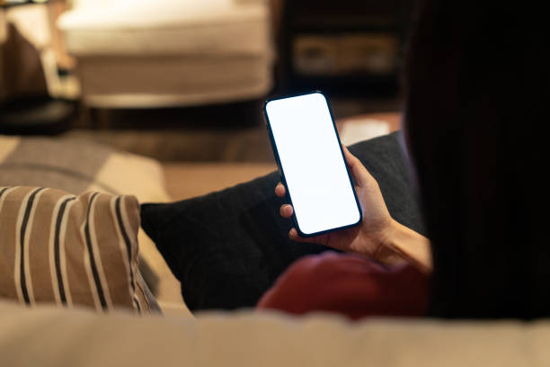 istock View from behind a person using a smartphone with a blank screen, in a warmly lit, comfortable home interior setting. 2149690168