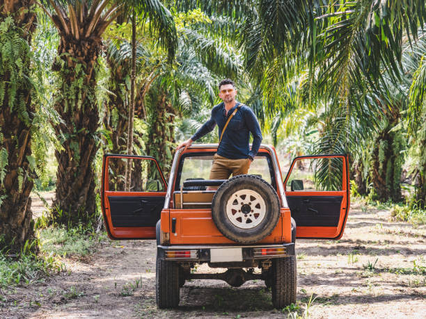 Attractive man and a red SUV against a background of palm trees. Sunny, clear day. Closeup, outdoors. Vacation and travel concept