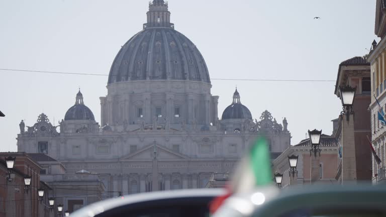 Italian flag fluttering on wind at Via della Conciliazione, Road of Conciliation leading to the Vatican St Peter Square and Basilica. Establishing cinematic shot