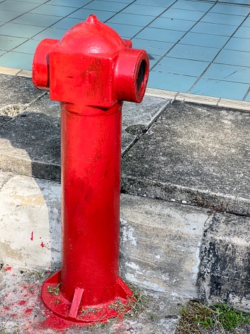 A classic red fire hydrant stands as a vibrant focal point against the muted tones of a city sidewalk. The hydrant, marked by time with subtle rust and wear, tells a story of urban life and reliability.