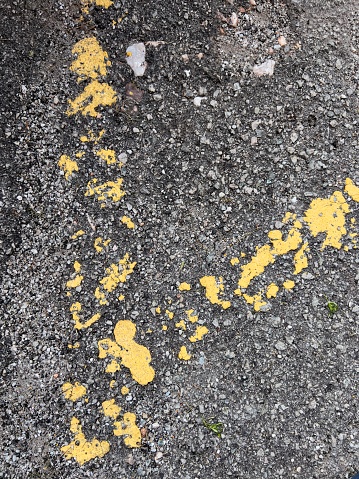 The essence of urban wear and tear, featuring the remnants of yellow road marking paint on a textured asphalt surface. The faded and chipped paint tells a story of countless vehicles that have passed over it, leaving behind a patchwork of history.