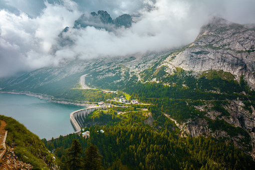 Summer time in Dolomites. landscape with mountains, Fedaia lake, clouds and forest.