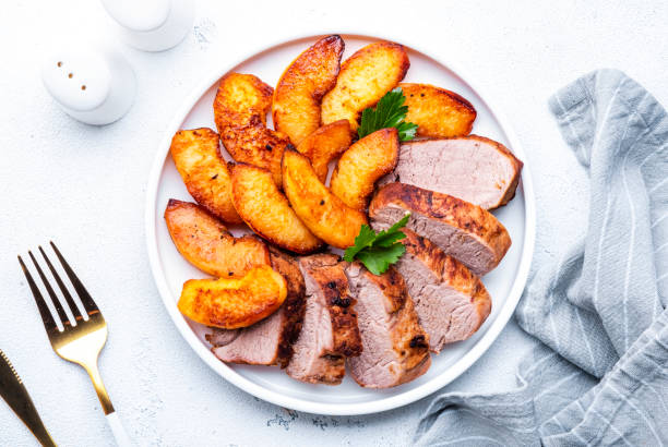 istock Baked pork tenderloin with caramelized apples on plate, white table background, top view 2149693707