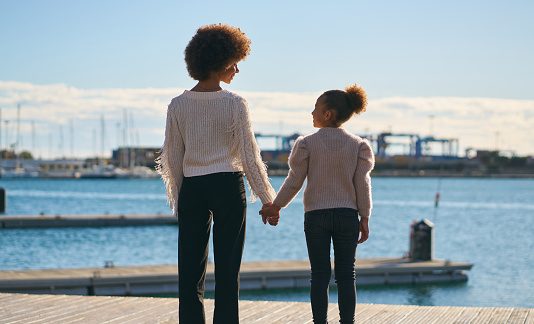 A woman and a child are standing on a dock by the water. The woman is holding the child's hand