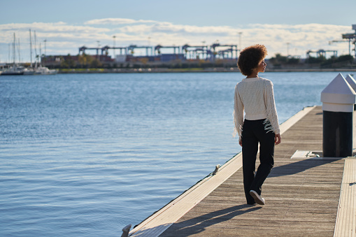A woman is walking on a dock by the water. The water is calm and the sky is clear