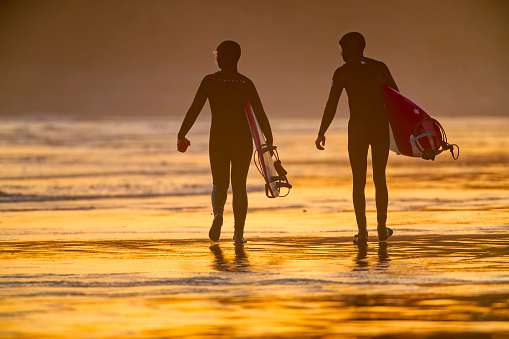 The Pacific Rim National Park on Vancouver Island on April 26, 2023:  Two female friends exiting the ocean after a surfing session at Pacific Rim National Park on Vancouver Island at sunset, British Columbia