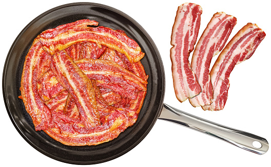 Traditional gourmet bunch of freshly fried crunchy bacon rashers, prepared in the large, heavy duty, non-stick ceramic coated black frying pan, combined with three meaty, streaky boiled pork belly bacon slices, isolated on white background, viewed directly above, high resolution stock image.