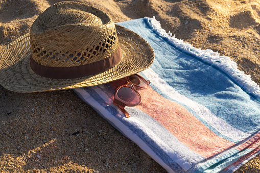 Summer backgrounds: beach sandals, sunglasses, beach mat and sun hat shot from above on sand background. A starfish complete the composition. The composition is at the right of an horizontal frame leaving useful copy space for text and/or logo at the left. High resolution 42Mp outdoors digital capture taken with SONY A7rII and Zeiss Batis 40mm F2.0 CF lens