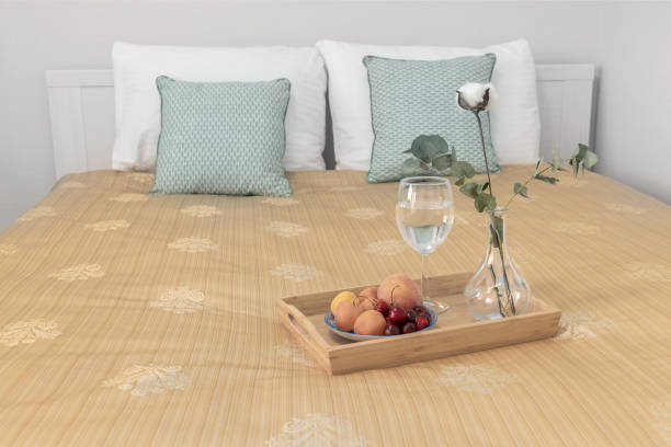 istock Interior with a bed adorned with pillows, a table with fruits, water, and a vase with eucalyptus in the background. 2149704436