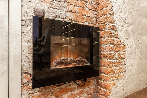 Interior with a wall-mounted electric fireplace against a brick and plastered wall.