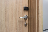 Wooden door with a metal handle and electronic key reader against a gray background.