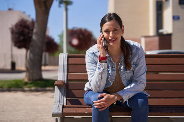 istock Beautiful woman talking on the phone while seated on a bench 2149705081