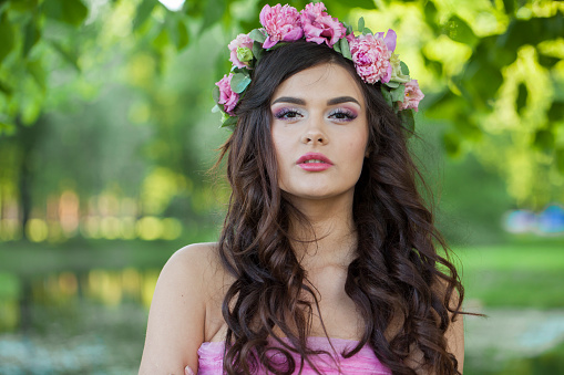 Charming healthy woman with makeup and long wavy dark brown hairstyle with flowers on head in spring park outdoor