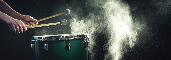 A man plays a musical percussion instrument with sticks on a dark background. Web, social media banner template.