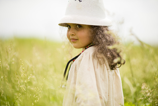 Cute baby girl in white dress and panama hat in summer holds a bouquet of delicate wildflowers in the forest.