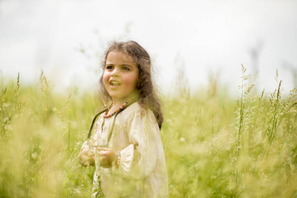 A young woman in white dress sitting on the ground, cutting flowers, having a picnic outside on a meadow during summer autumn season. Cottagecore, rustic, farmcore aesthetics concept.