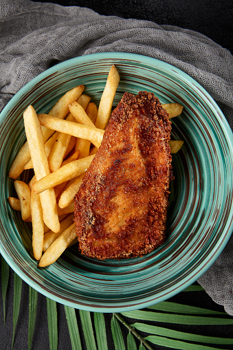 Chicken tenders with french fries in bowl on black backdrop. Junk food on dark stone background. Crispy chiken fillet with potatoes in minimal style. Combo with fried chicken breast and potatoes