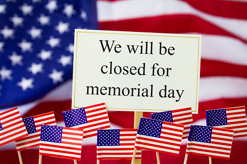 We will be closed for Memorial Day written on a white sign with an American flag behind and small American flags in the foreground.