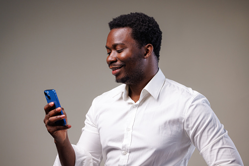 Waist up shot of a young African American man in a white shirt, using a mobile phone