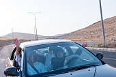An Arabic family, dressed in traditional attire, smiles happily in a car, showing thumbs-up signs. They seem excited for a fun picnic adventure together
