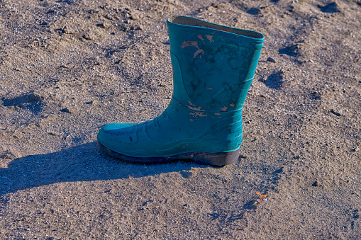 Abandoned rubber old boot of green color on the background of a sandy surface top view.
