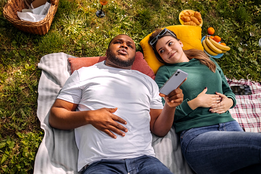 Couple enjoying on picnic in the spring lying on back and using smart phone