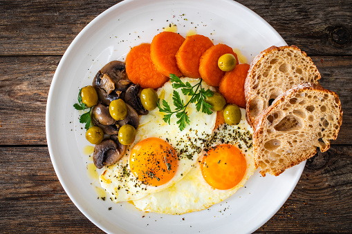 Breakfast - sunny side up egg, toasted bread, sweet potato, mushrooms and olives served on wooden table