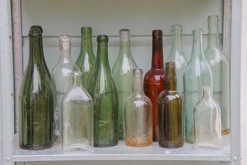 old empty bottles of various capacities and colors on an iron shelf