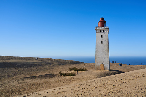 Lønstrup, Denmark. February 28, 2021. Rubjerg Knude lighthouse on sandy mountain with beautiful sea and horizon in background under clear blue sky during sunny day