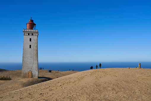 Lønstrup, Denmark. February 28, 2021. Rubjerg Knude lighthouse on sand dunes coast with idyllic North Sea and horizon in background against clear blue sky during summer