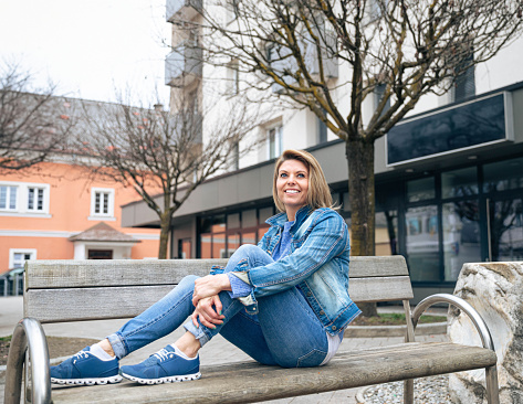 Woman lounging on bench, wearing blue denim attire, looking thoughtful