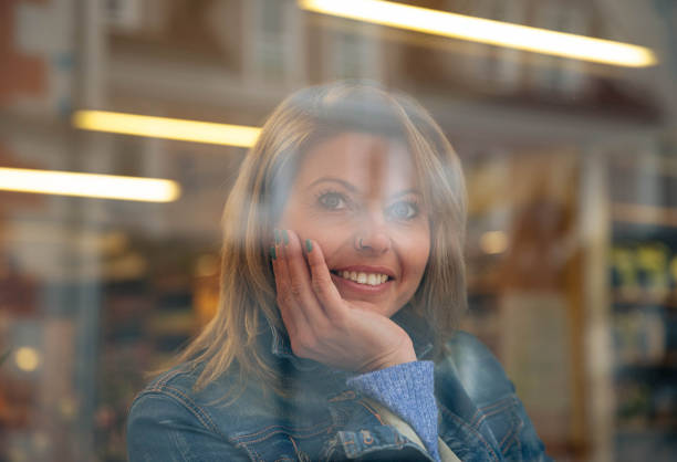 Joyful woman in denim, seen through glass with light reflections