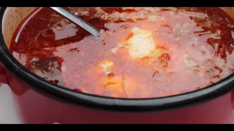 Traditional Slovak Ukrainian Russian cabbage soup with sausage and smoked meat in retro red metal pot served on the plate with spoon. Bowl of delicious Soljanka borsch with white sour cream. Top view